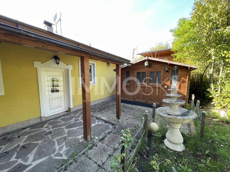 Gelbes Haus mit überdachtem Eingangsbereich, Steinfliesen und einem dekorativen Brunnen im Garten.