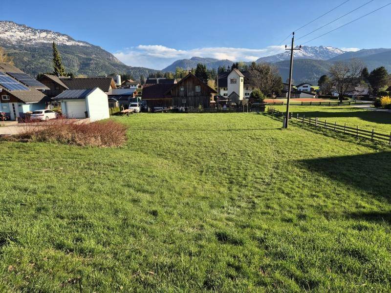 Weitläufiges grünes Grundstück mit Blick auf die umliegende Bebauung und schneebedeckte Berge.