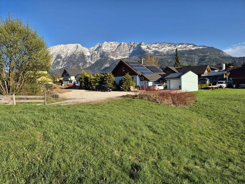 Sonniger Blick über ein grünes Grundstück auf Häuser und majestätische schneebedeckte Berge.