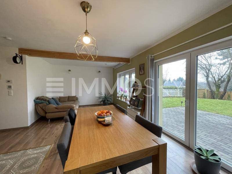Geräumiger Wohn-Essbereich mit Holztisch, Sofa und Zugang zur Terrasse mit Gartenblick.