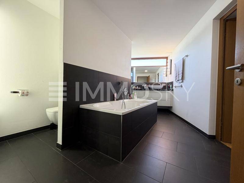 Modernes Badezimmer mit dunklen Fliesen, eingebauter Badewanne und Doppelwaschbecken.