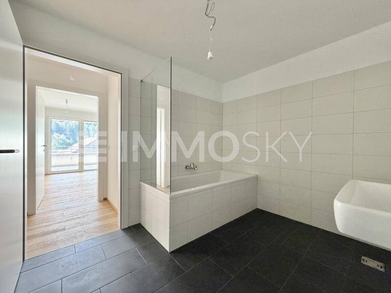 Modernes Badezimmer mit dunklen Fliesen, Badewanne mit Glasabtrennung und Wandwaschbecken.