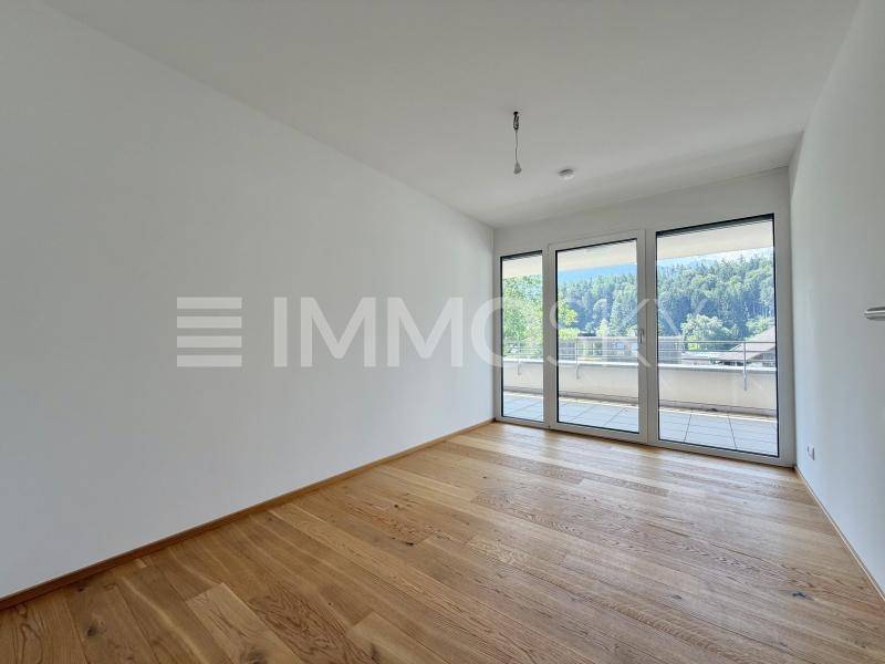Geräumiges Schlafzimmer mit Holzboden und Zugang zu einem sonnigen Außenbereich durch große Fenster.
