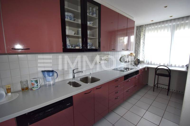 Moderne Einbauküche mit glänzenden rosa Fronten, integrierten Geräten und einem Fenster.
