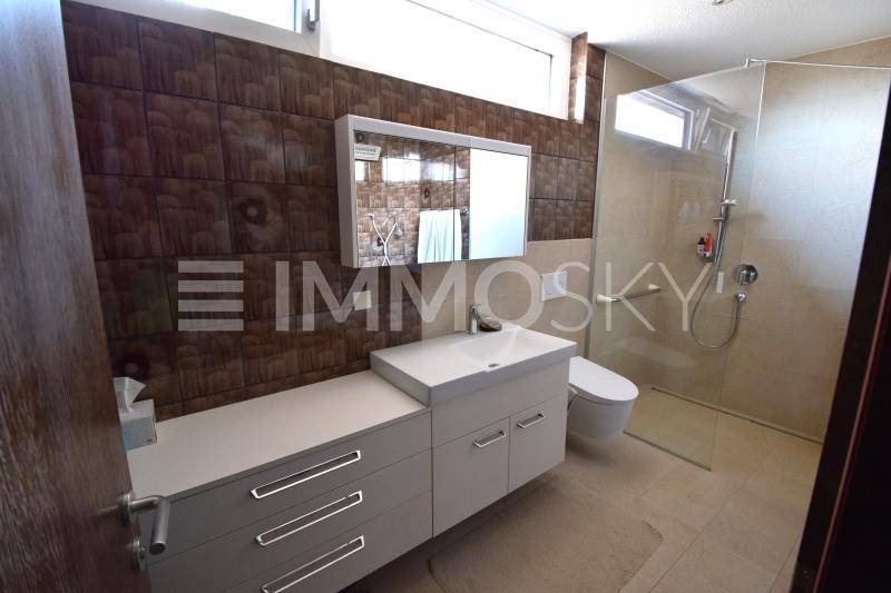 Modernes Badezimmer mit begehbarer Dusche, Waschtischunterschrank und braunen Wandfliesen.