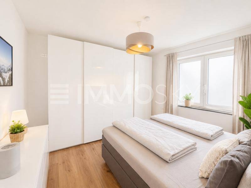 Helles Schlafzimmer mit Doppelbett, weißem Kleiderschrank und Holzboden.