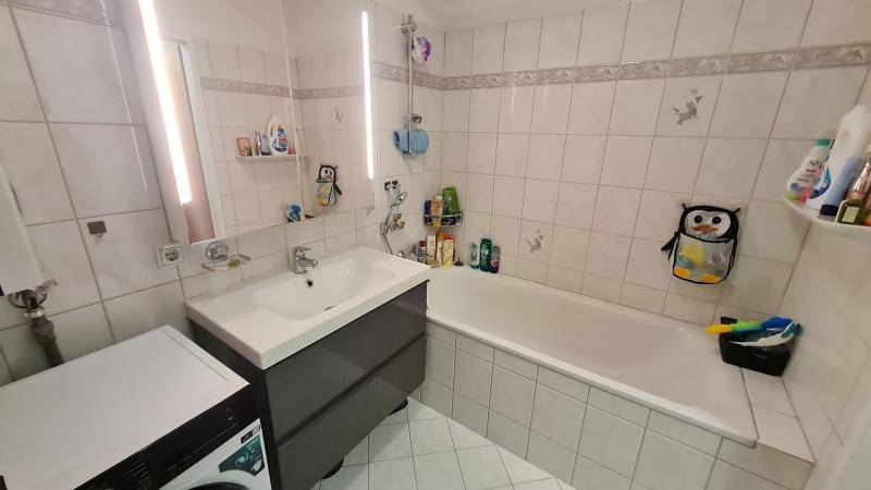 Gefliestes Badezimmer mit Badewanne, Einzelwaschbecken und Waschmaschine.