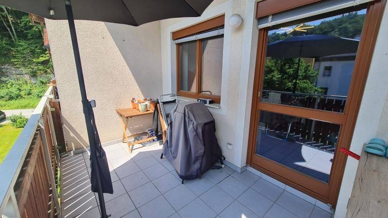 Gemütlicher Balkon mit Fliesenboden, Sonnenschirm und Blick ins Grüne.