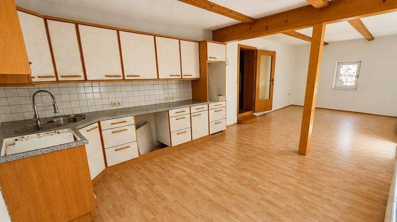 Helle Küche mit hellen Holzschränken und Fliesen, offen zu einem Raum mit Holzbalken.