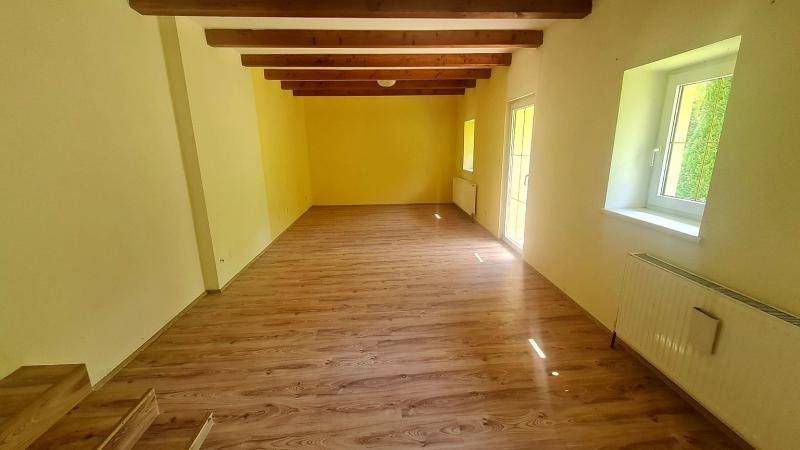 Geräumiger Raum mit gelben Wänden, sichtbaren Holzbalken und Laminatboden.
