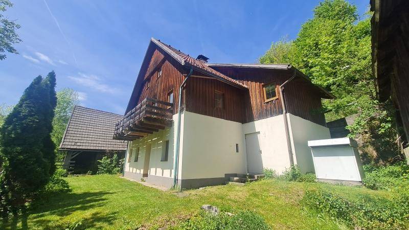 Traditionelles Haus mit Holzfassade und Balkon, umgeben von einem grünen Garten.