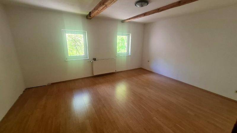 Heller Raum mit weißen Wänden, sichtbaren Holzbalken und Laminatboden.