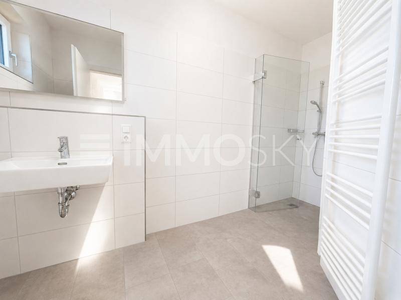 Modernes Badezimmer mit weißen Fliesen, ebenerdiger Dusche und beheiztem Handtuchhalter.