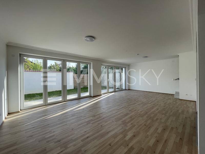 Geräumiges Wohnzimmer mit hellem Holzboden und großen Fensterfronten zum Garten.