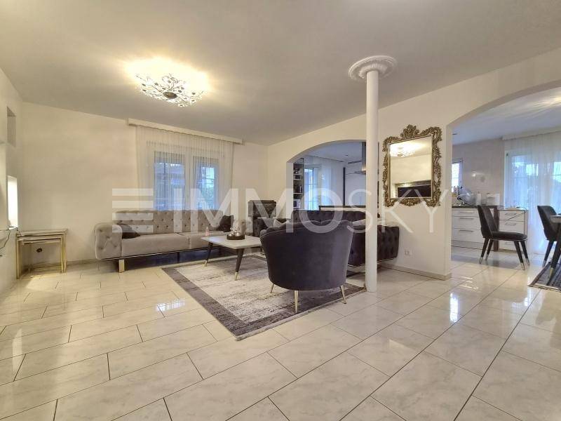 Geräumiges Wohnzimmer mit eleganten Möbeln, Fliesenboden und offenem Übergang zum Essbereich.