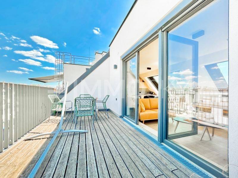 Geräumige Holzterrasse mit Sitzgelegenheiten und Zugang zu einem hellen Innenraum mit gelbem Sofa.