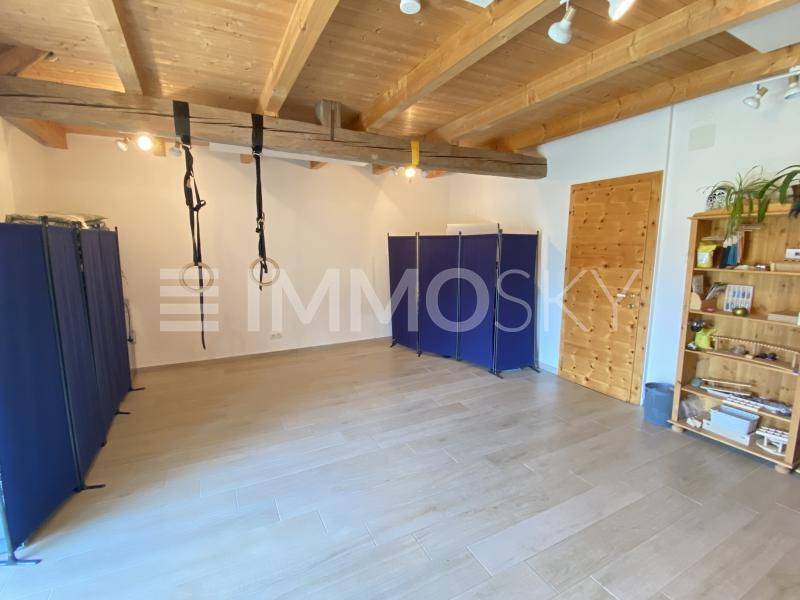 Geräumiger Fitnessraum mit sichtbaren Holzbalken an der Decke, hellem Fliesenboden und Trainingsgeräten.