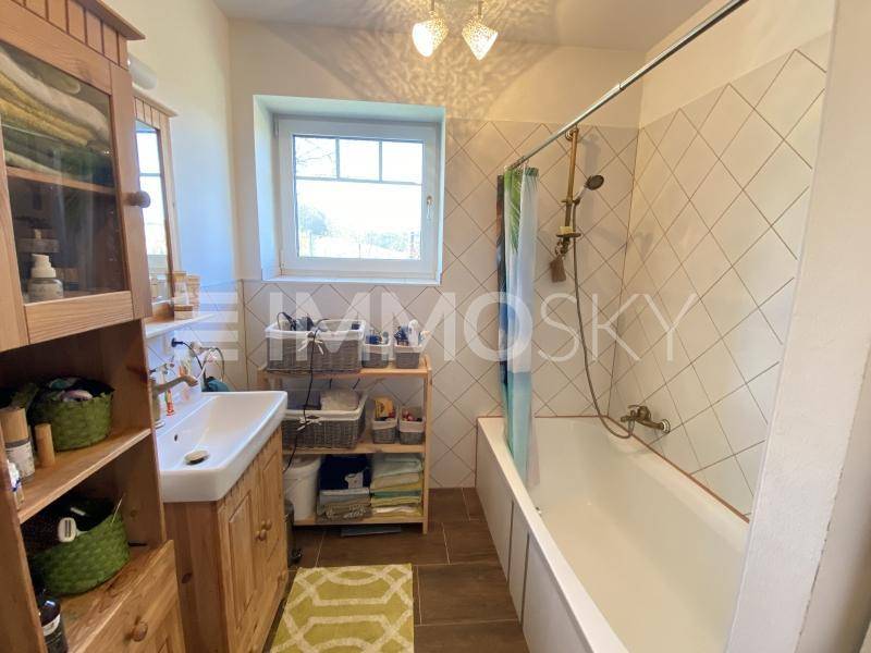 Funktionales Badezimmer mit Badewanne, Einzelwaschbecken, Fenster und Holzschrank für Stauraum.
