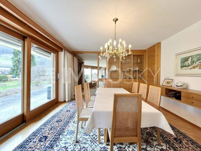 Eleganter Essbereich mit Holztisch, Korbstühlen und Kronleuchter, mit Zugang zum Außenbereich.