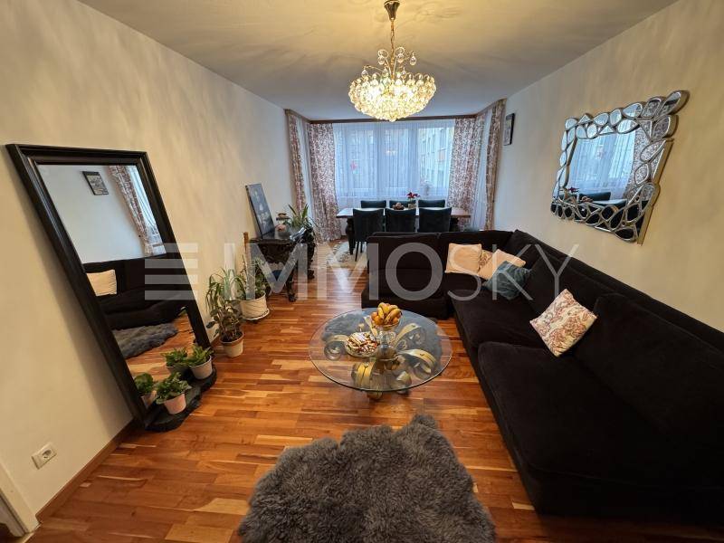 Geräumiger Wohn-Essbereich mit dunklem Sofa, Kronleuchter und dekorativen Spiegeln, verbunden mit dem Essbereich.