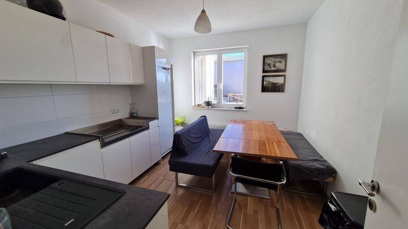Kleine Küche mit weißen Schränken, einem Holztisch, einer Sitzbank und einem Fenster, das Tageslicht spendet.
