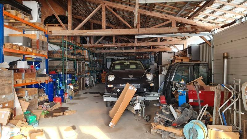 Unordentliche Garage oder Lagerbereich mit sichtbaren Holzsparren, einem geparkten Auto und verschiedenen Gegenständen.