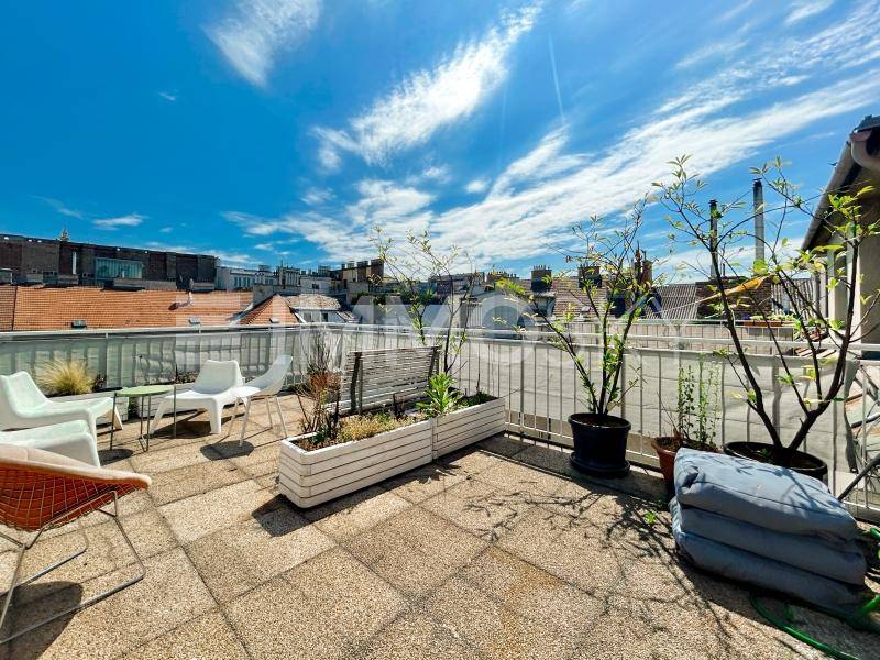 Geräumige Dachterrasse mit Fliesenboden, Pflanzen und Sitzgelegenheiten unter strahlend blauem Himmel.