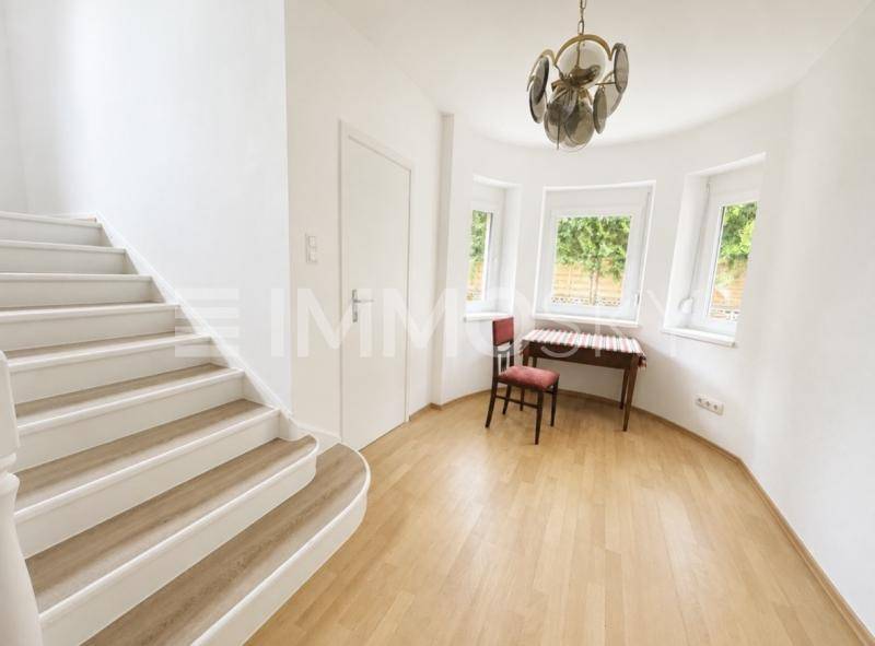 Heller Flur mit geschwungener Treppe, Parkettboden und Erkerfenstern.