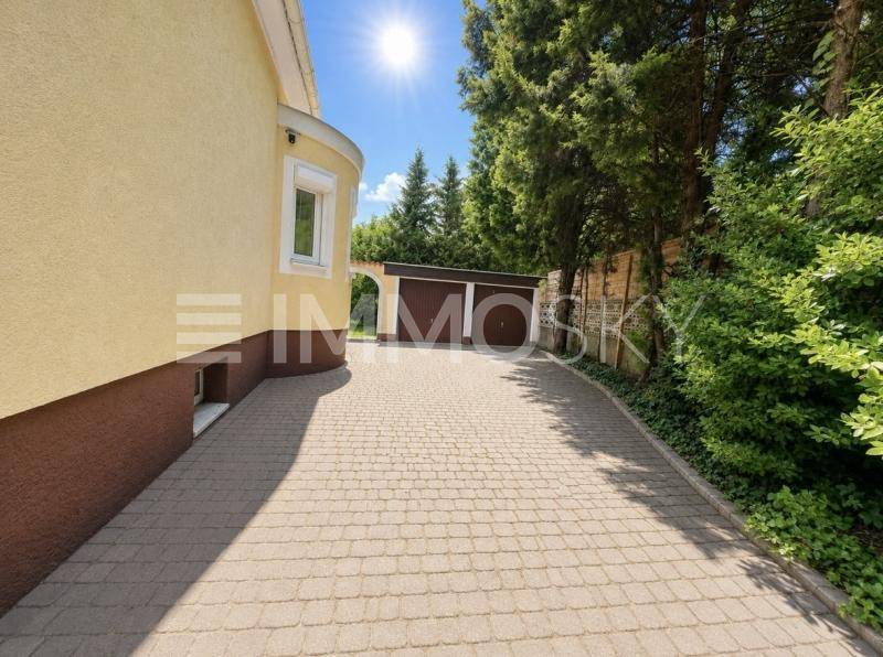 Gepflasterte Einfahrt neben dem Haus, umgeben von grünen Bäumen und Sträuchern.