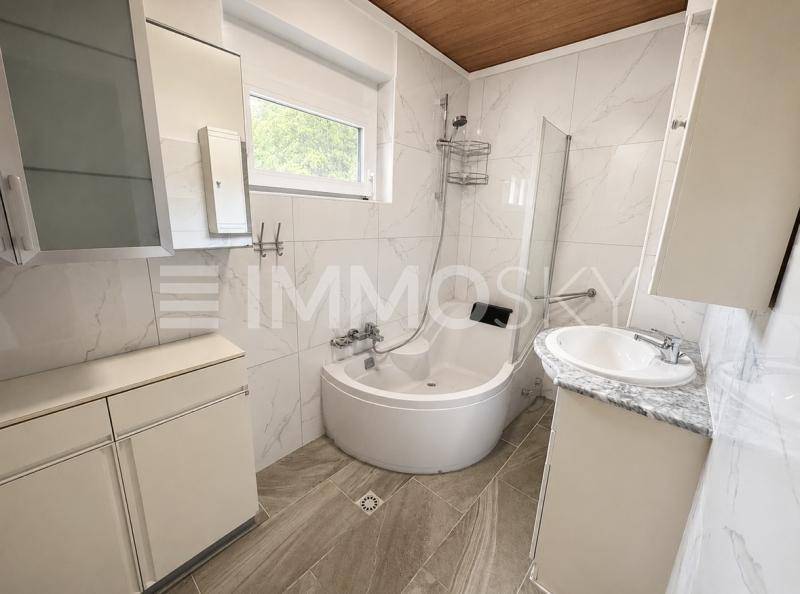 Helles Badezimmer mit modernen Fliesen, Eckbadewanne und Fenster.