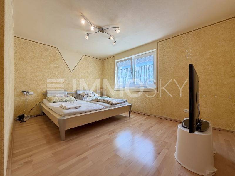 Helles Schlafzimmer mit Parkettboden, Doppelbett und Fenster für natürliche Belichtung.