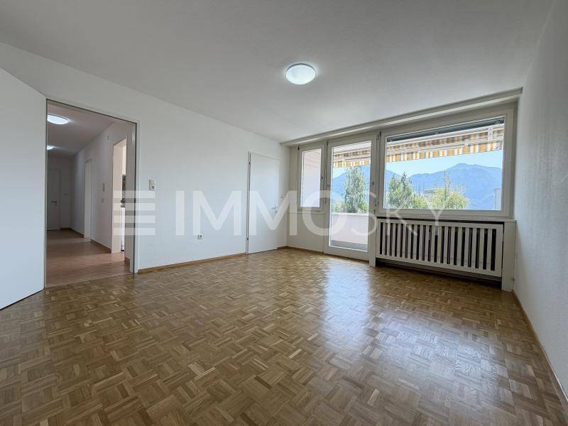 Helles Wohnzimmer mit Parkettboden, Zugang zum Balkon und Bergblick.