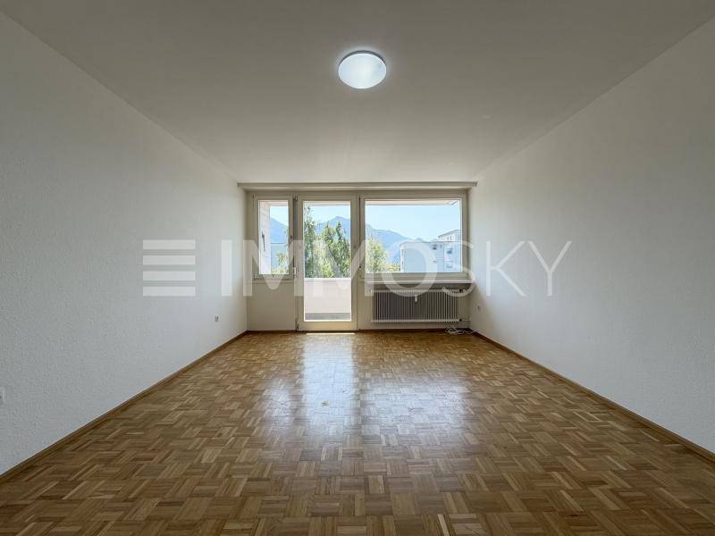 Geräumiges Wohnzimmer mit klassischem Parkettboden und großem Fenster mit Bergblick.
