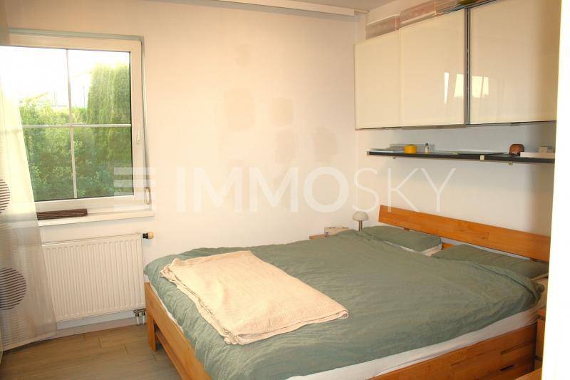 Schlichtes Schlafzimmer mit Holzbett, weißen Wänden und Fenster mit Blick ins Grüne.