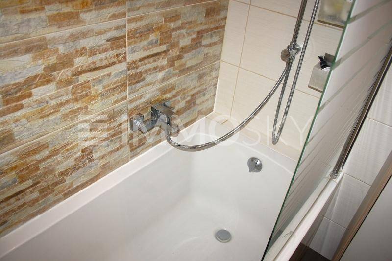 Badezimmer mit Badewanne und Duschfunktion, gefliest mit Steinoptik und weißen Fliesen.