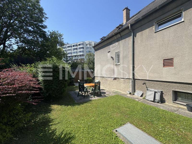 Gepflegter Gartenbereich hinter dem Haus mit Rasenfläche und einer kleinen Sitzgelegenheit.