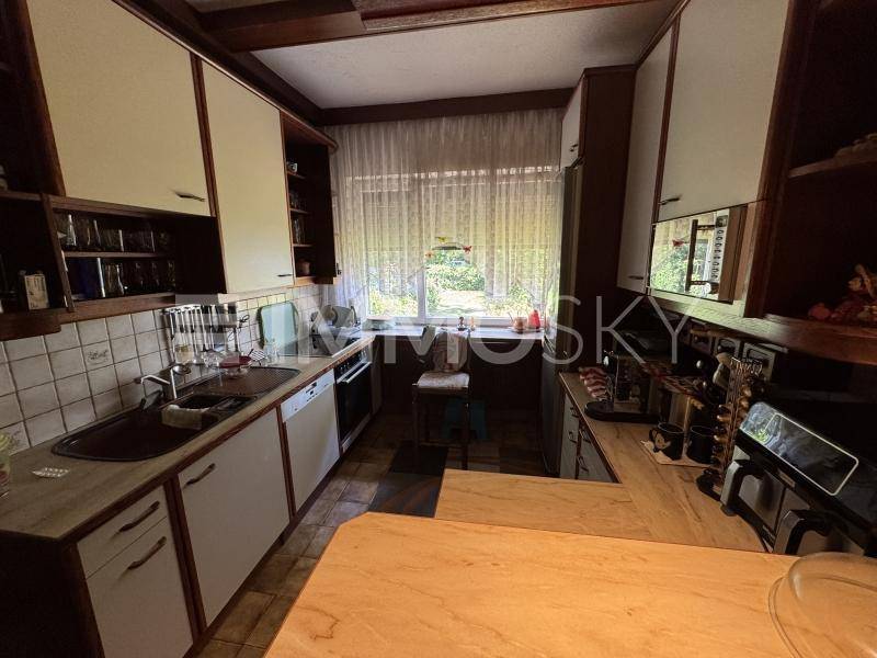 Funktionale Küche mit Holzschränken, gefliestem Spritzschutz und Fenster mit Blick ins Grüne.