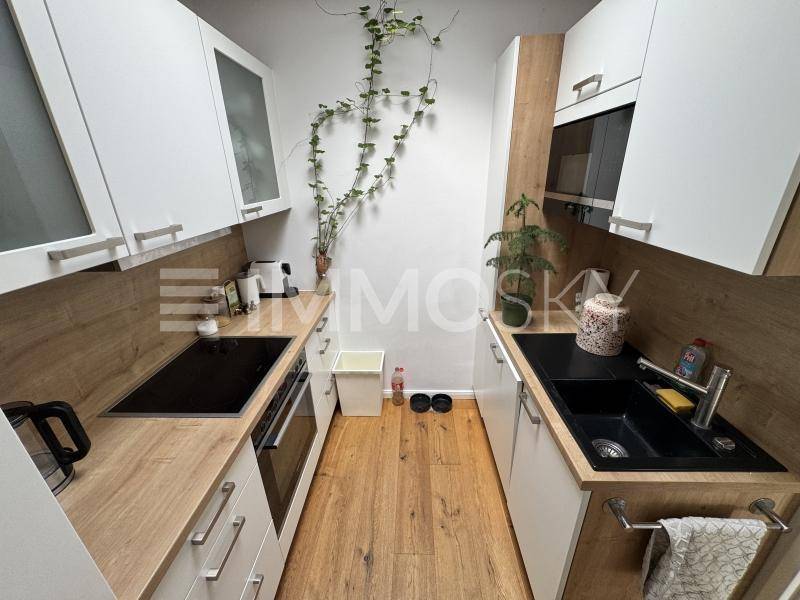Schmale, moderne Küche mit weißen Schränken, Holz-Arbeitsplatten und Induktionskochfeld.