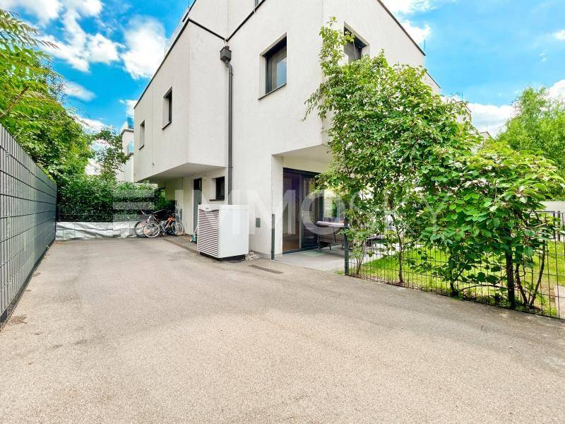 Moderne Gebäudefassade mit Zufahrt und grüner Bepflanzung, die Privatsphäre bietet.