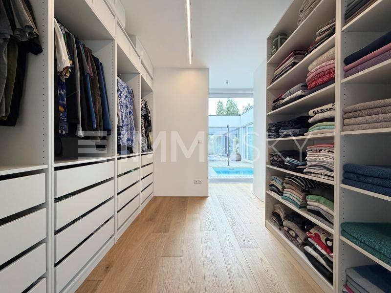 Geräumiger begehbarer Kleiderschrank mit maßgefertigten Einbauschränken und Poolblick.