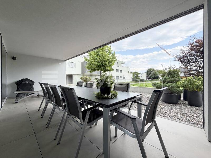 Geräumige überdachte Terrasse mit Esstisch und Blick auf die umliegende moderne Bebauung.