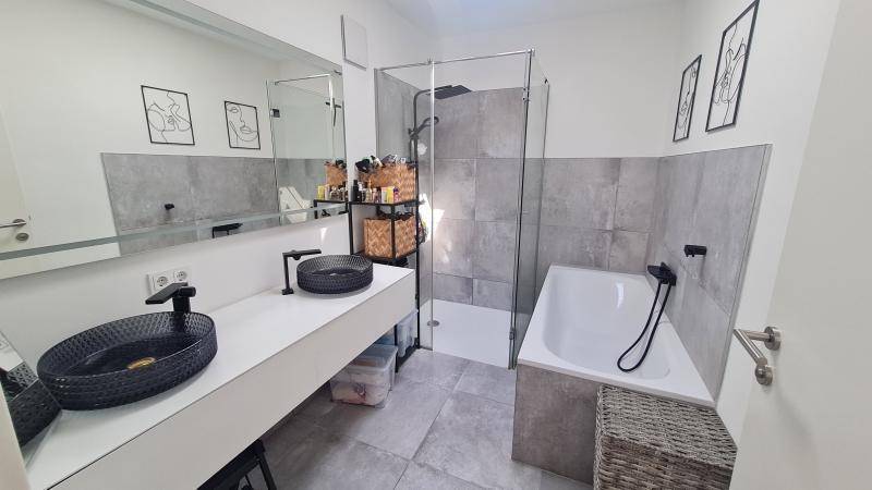 Modernes Badezimmer mit grauen Fliesen, Badewanne, Dusche und Doppelwaschbecken.