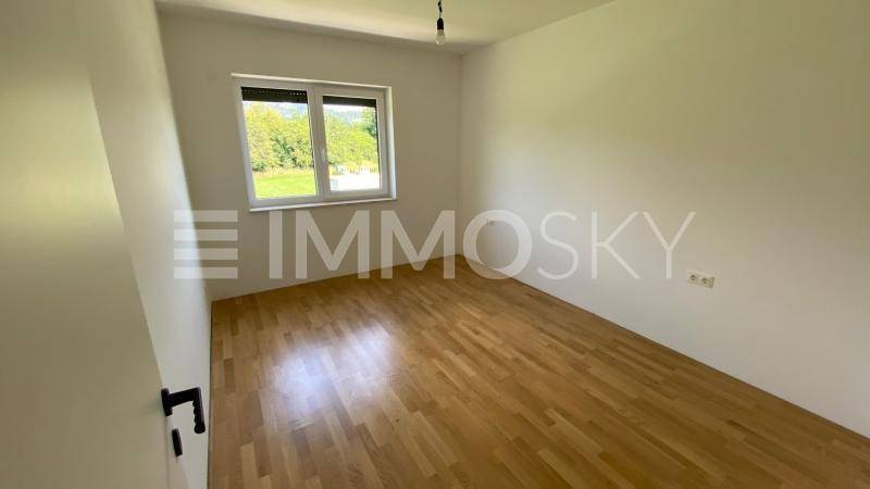 Leeres Schlafzimmer mit Holzboden, einem Fenster und Blick auf die Natur.