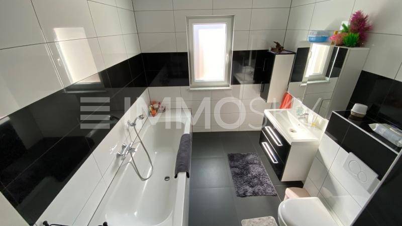 Modernes Badezimmer mit schwarz-weißen Fliesen, Badewanne, Waschbecken und Fenster.