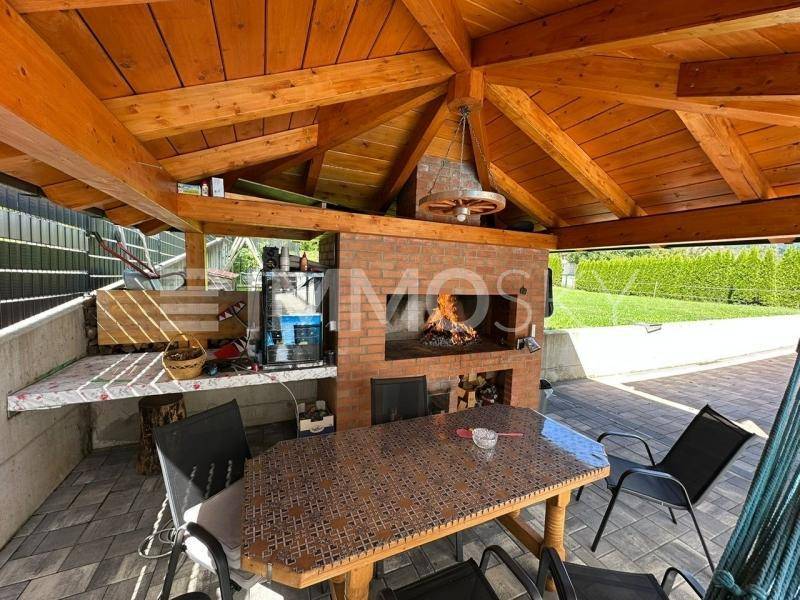 Überdachte Terrasse mit gemauertem Grillkamin und Holzbalkendecke für gemütliche Abende.