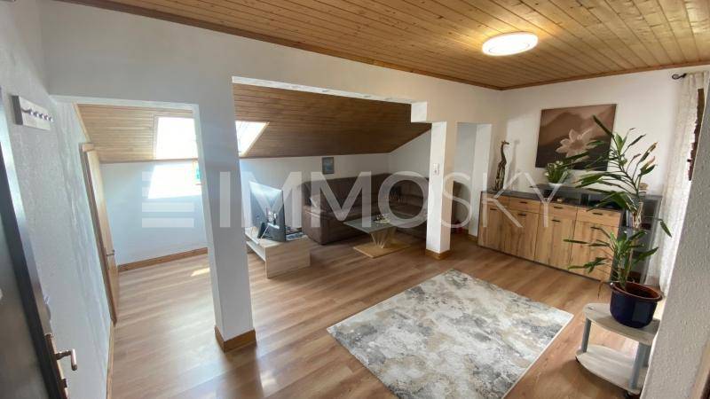 Gemütlicher Wohnbereich mit Holzdachschrägen, Laminatboden und einem Sofa im hinteren Bereich.