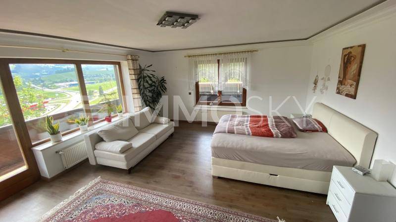 Helles Schlafzimmer mit Bett, Sofa und großen Fenstern mit weitem Blick ins Grüne.