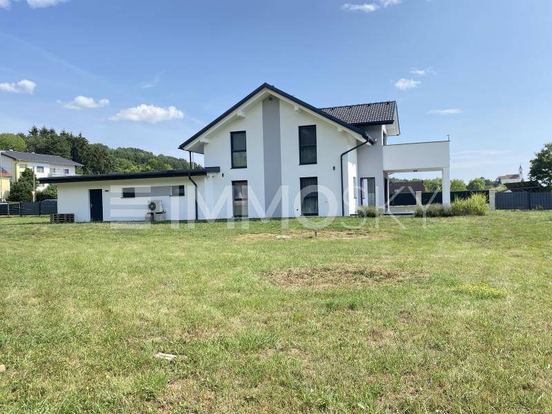 Weitläufiges Grundstück mit modernem Einfamilienhaus und viel Grünfläche unter blauem Himmel.