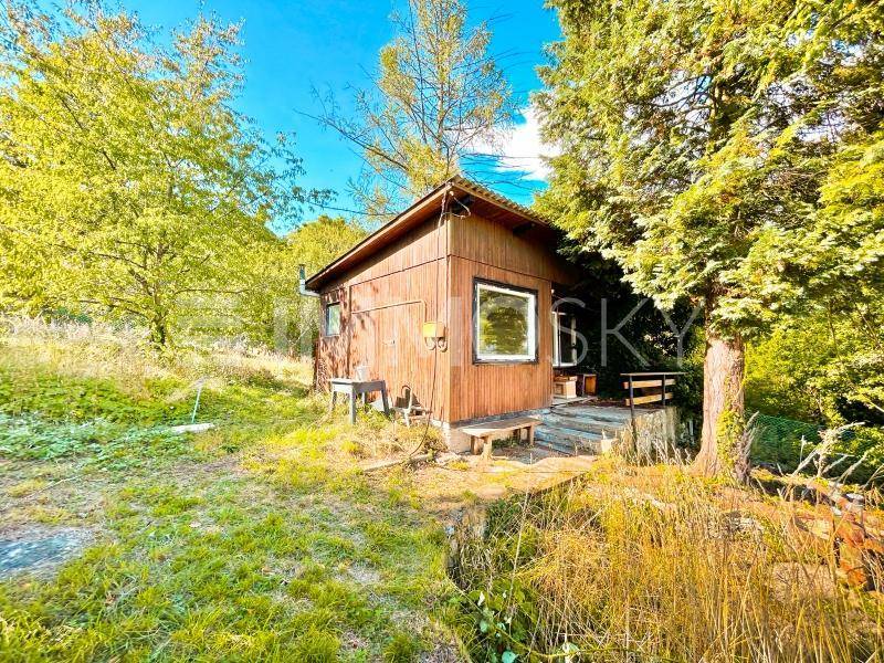 Rustikale Holzhütte mit kleiner Veranda und Sitzbank, eingebettet in einen grünen Gartenbereich.