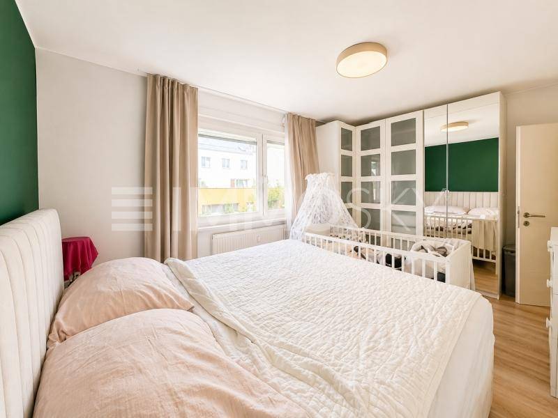 Schlafzimmer mit Doppelbett, Kinderbett und großem Spiegelschrank, hell und freundlich.